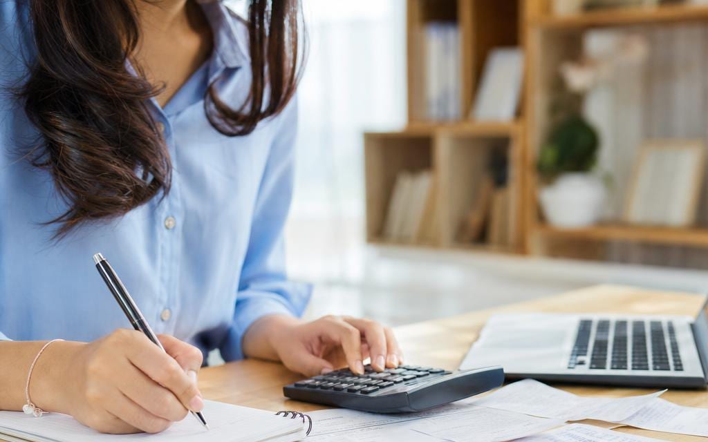 A person adding up filing costs on a notepad beside a calculator and receipts